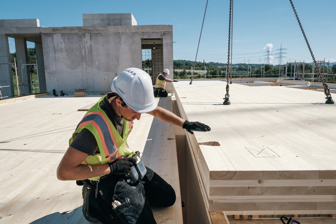  Arbeiter auf einer Baustelle beim Ausrichten eines CLT-Deckenpaneels