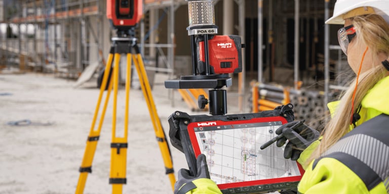 Frau auf der Baustelle mit Hilti Tablet und Totalstation beim Vermessen