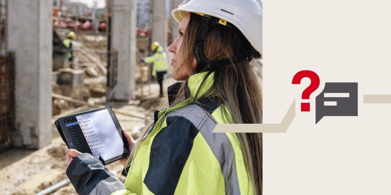 Eine Frau steht vor der Baustelle mit einem Tablet in der Hand.