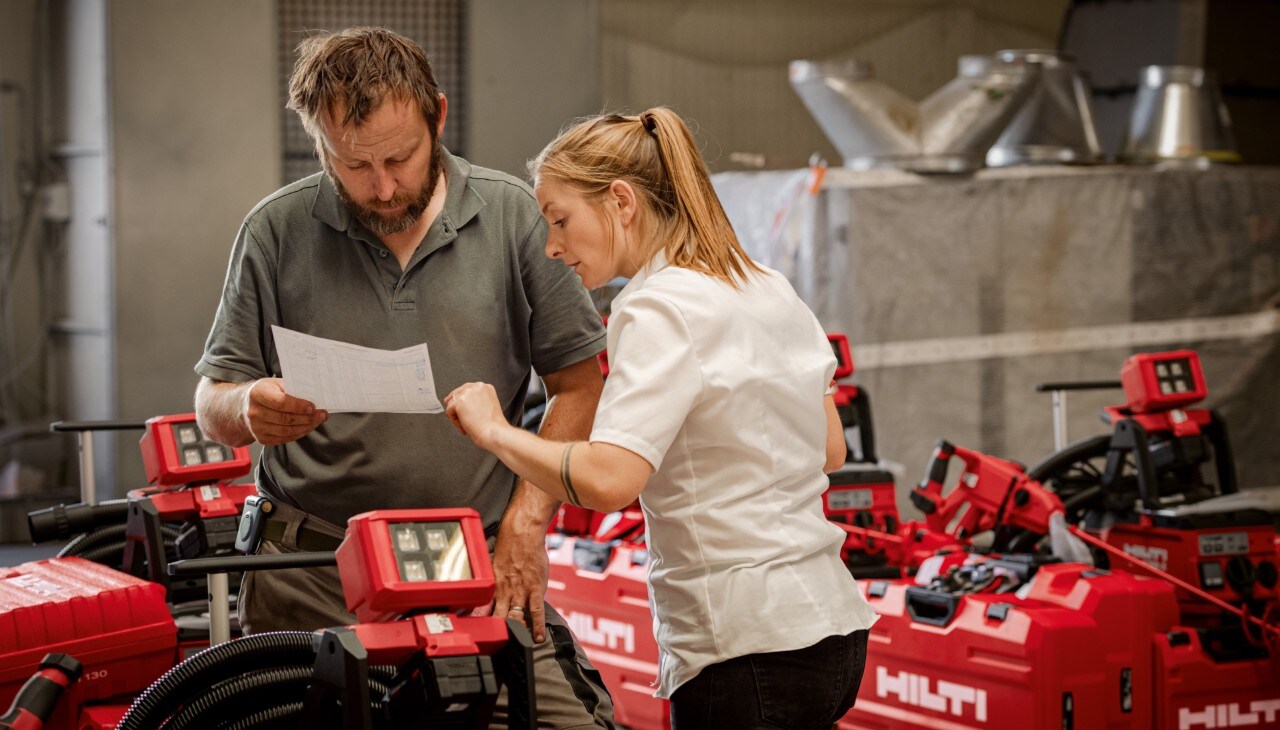 Eine Hilti Mitarbeiterin und ein Kunde prüfen Hilti Geräte in  einer Werkstatt.
