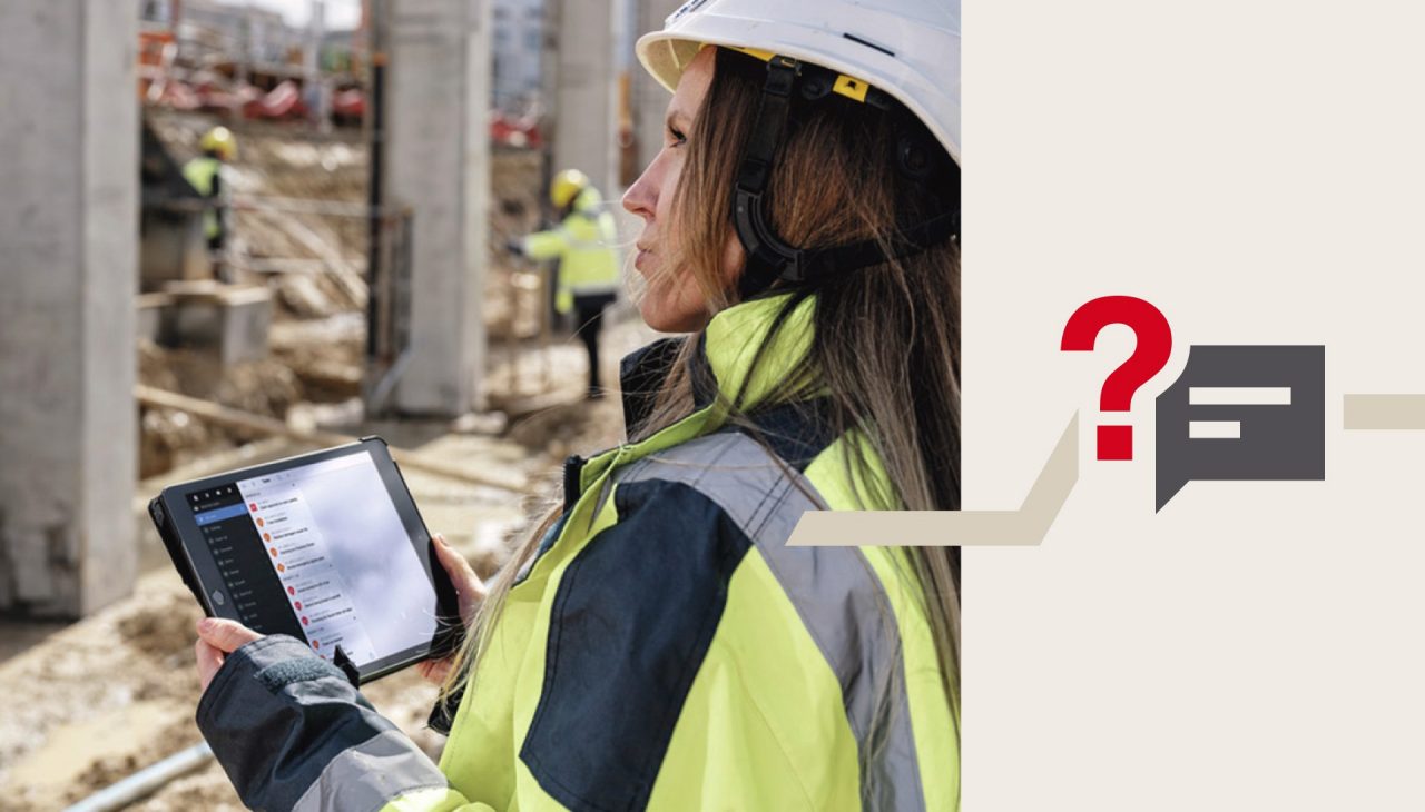 Eine Frau in Schutzkleidung mit Tablet in der Hand steht auf einer Baustelle und blickt prüfend.