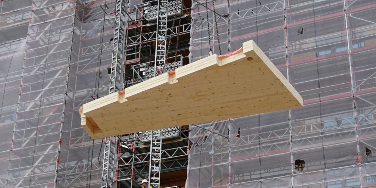 Ein Fertigbauteil aus Holz wird auf der Baustelle des “Roots” an Stahlseilen herabgelassen.
