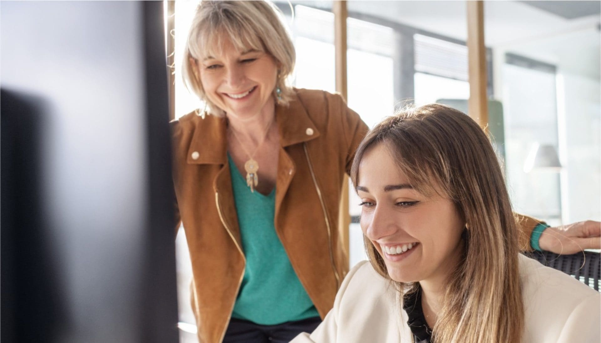 Zwei lächelnde Frauen im Büro vor einem Bildschirm.