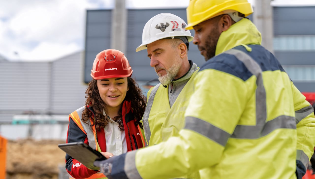 Drei Personen auf einer Baustelle schauen gemeinsam in ein Tablet.