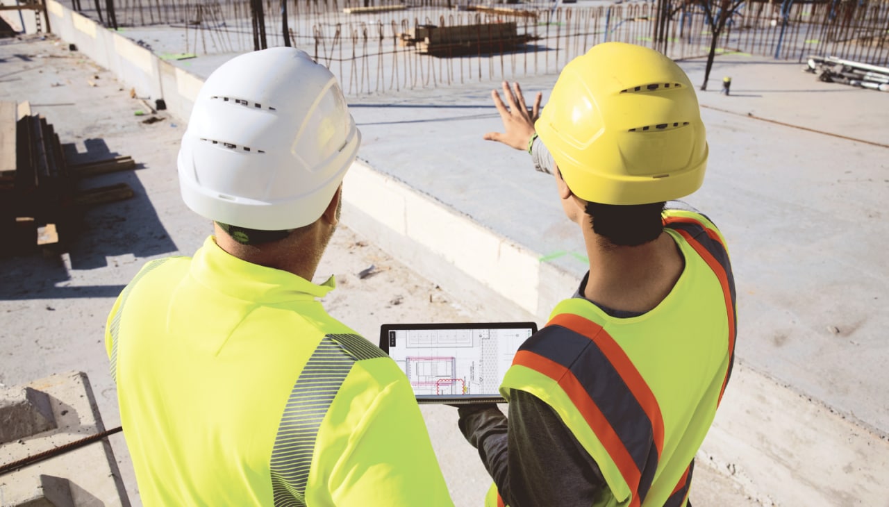 Zwei Personen auf einer Baustelle deuten in die Entfernung, eine Person hält ein Tablet mit Hilti Fieldwire Bausoftware in der Hand.