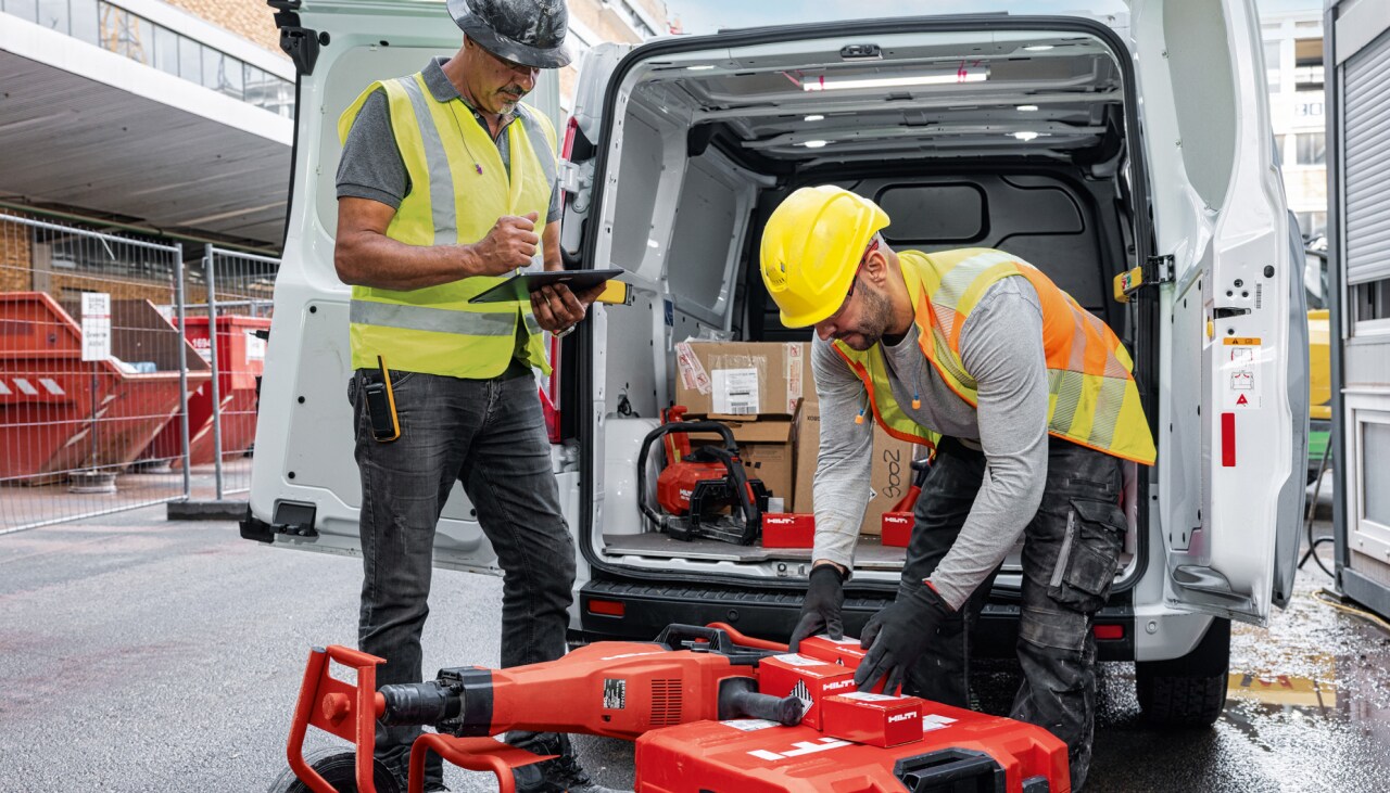 Zwei Personen vor einem geöffneten Lieferwagen, vor ihnen und im Wagen mehrere Kartons und Koffer mit Hilti Verbrauchsmaterial bzw. Geräten.