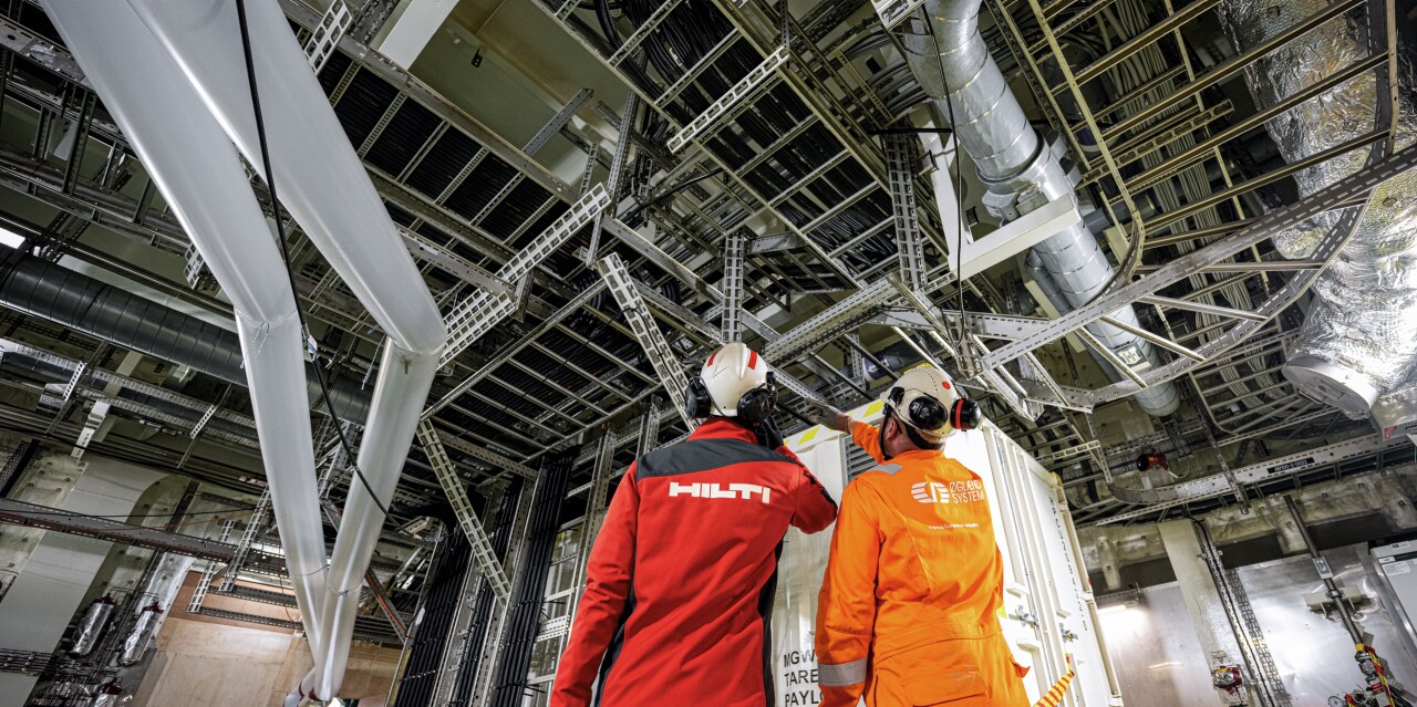 Zwei Arbeiter sind auf der Baustelle, einer davon trägt Kleidung der Marke Hilti.