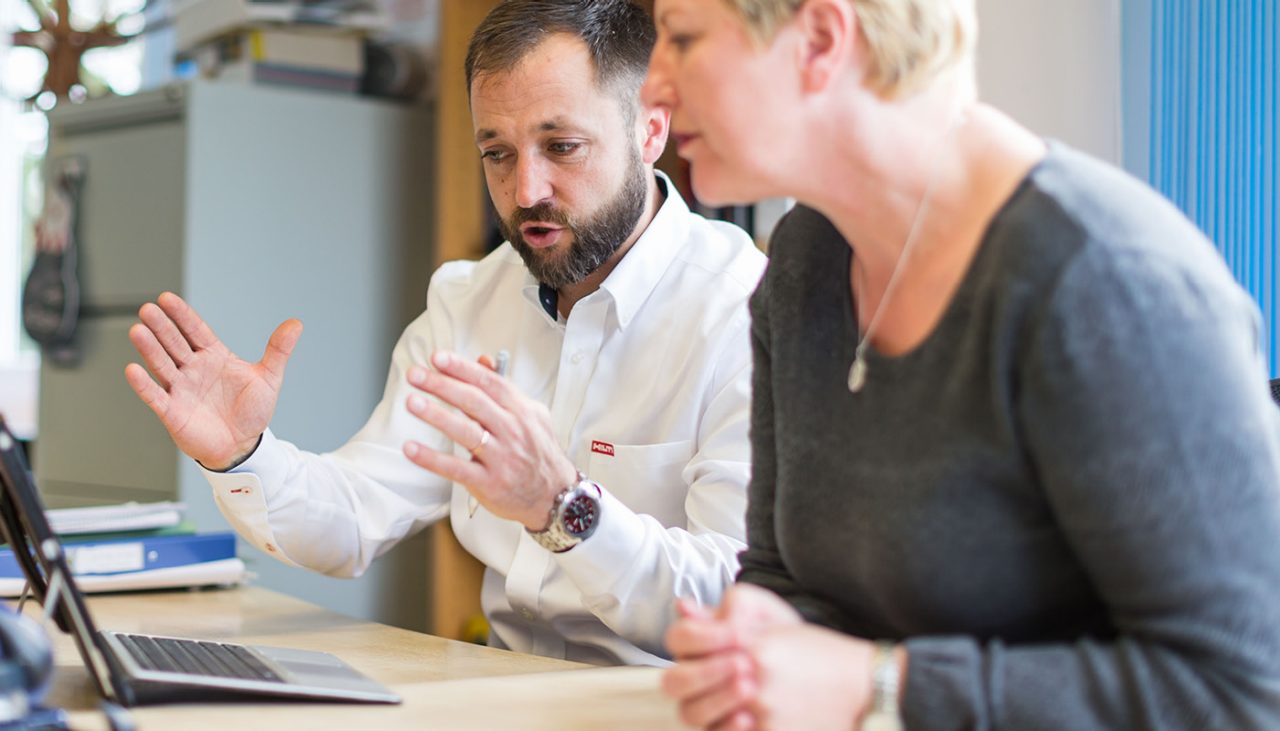 Ein Hilti Mitarbeiter und eine Mitarbeiterin diskutieren vor dem Laptop im Büro