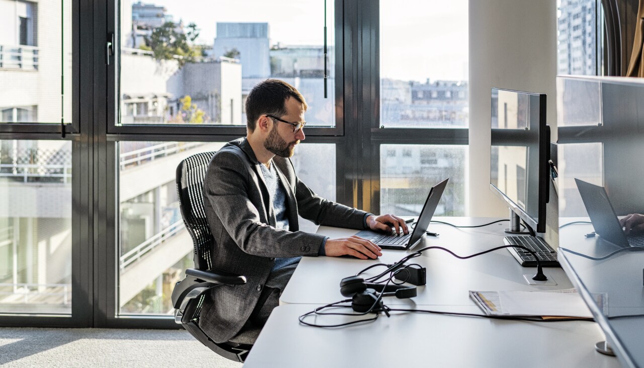 Ein Mann sitzt in einem Büro mit Glasfassade an seinem Laptop